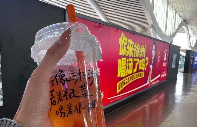  徐州东高铁站出发过了安检口前往站台的连廊两侧，蜜城之恋鸡蛋汤饮品创始人身着大红西装亮相