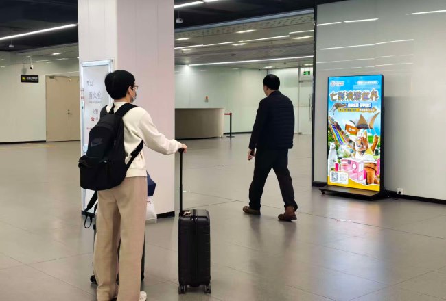 佛山机场航站楼到达空间，旅客为广佛文旅景区广告驻足停留观看信息