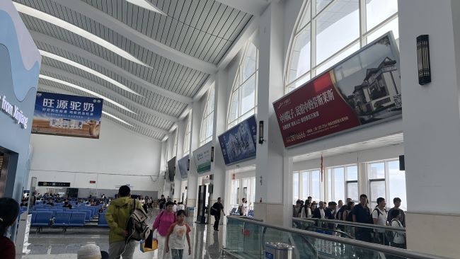 雪都机场候机厅旅客排队登机场景实拍图，候机厅上方刊登着羽绒服广告