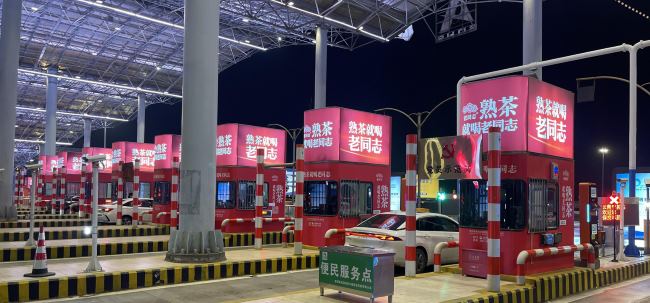 昆明机场高速收费站站亭一排有8个，图片是夜间场景拍摄的老同志熟茶站亭贴膜广告