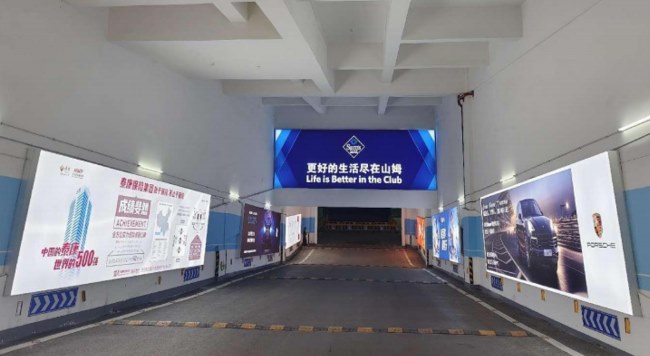 图为武汉光谷山姆华中旗舰店地下车库入口处场景实拍图，通道两侧灯箱广告画面分别为保时捷汽车和泰康保险