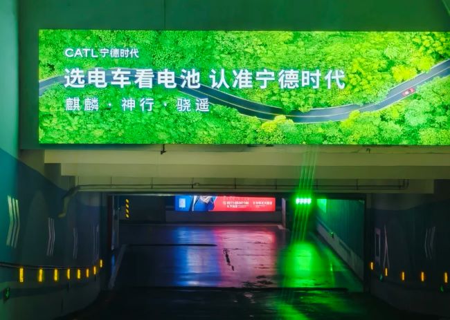 宁德时代选择地下停车场入口上方的楣头灯箱广告展示企业形象，绿色的广告画面在昏暗环境中格外醒目 
