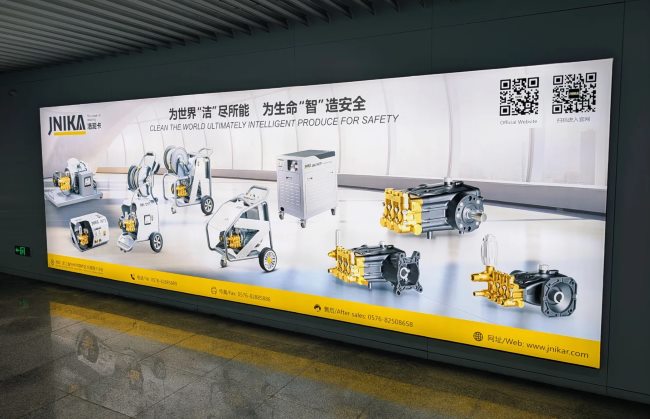 台州机场广告牌洁妮卡 (JNIKA) 清洗设备与泵头广告：展示了多台大型工业清洗机/高压水枪设备以及精密的黄色金属泵头零部件。